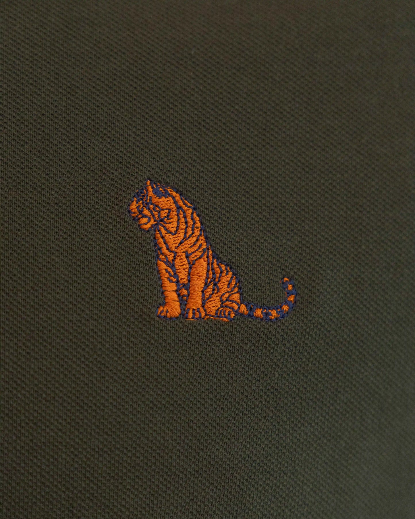 Close-up of an embroidered tiger on NAD's olive green cotton polo t-shirt for men.