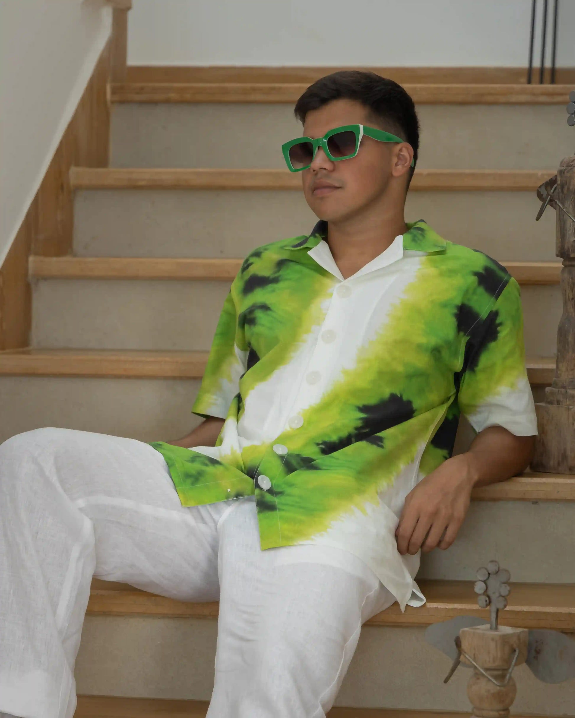 A man wearing NAD's green tie-dye shirt for men is seated on stairs, exuding a laid-back vibe.