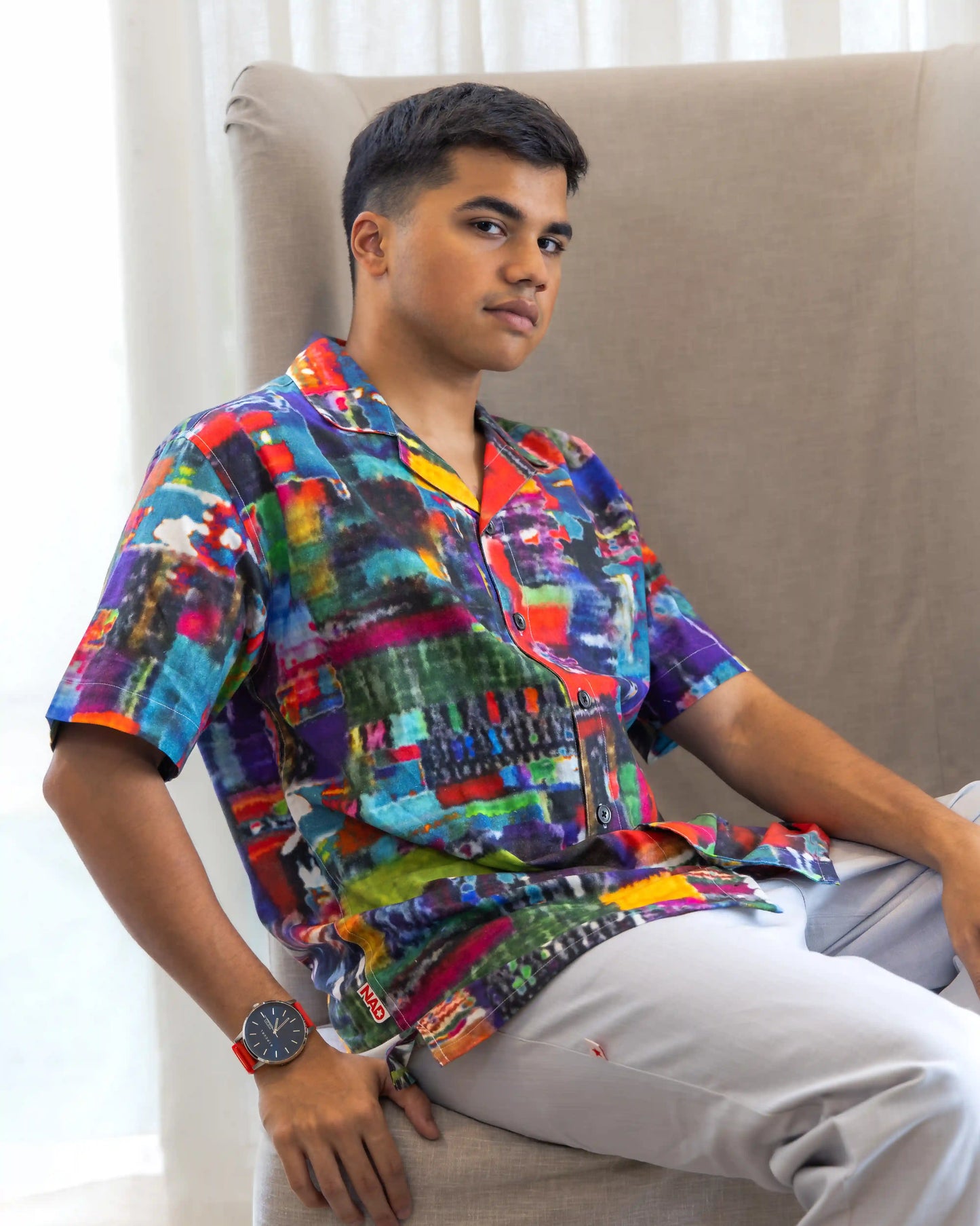 A model seated, showcasing NAD's abstract multi-coloured printed shirt for men.