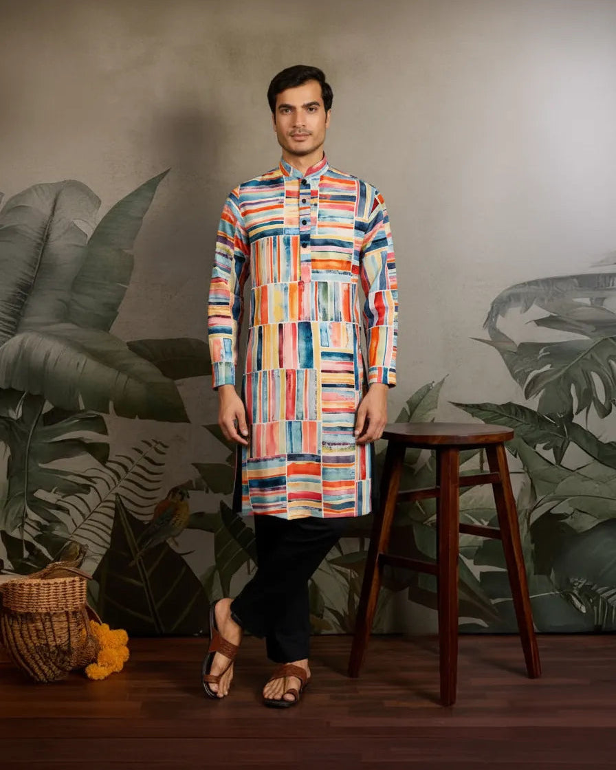 Man wearing a colorful kurta standing next to a wooden stool with a leafy background