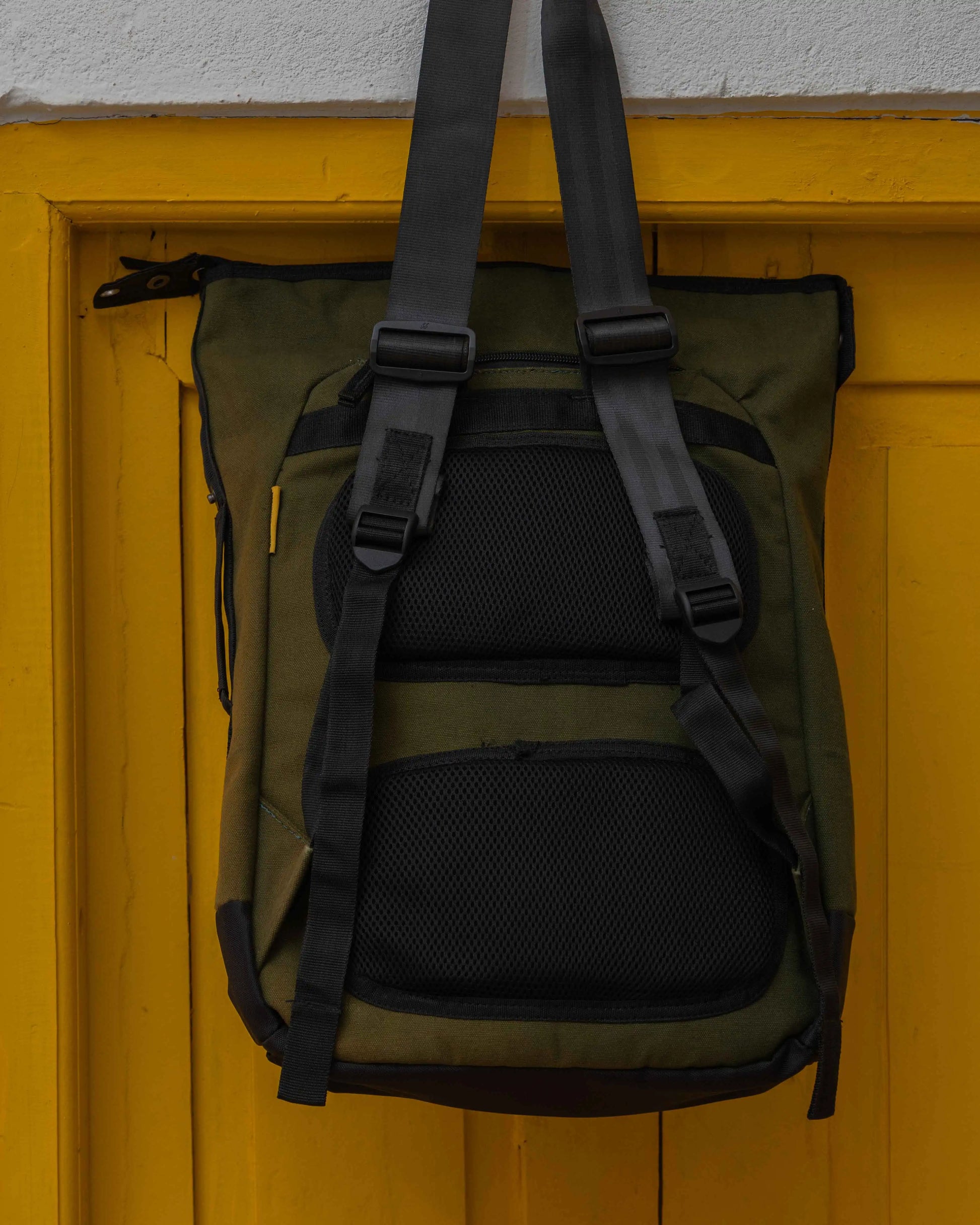 NAD's green bag for men on a yellow door, showcasing the Army Canvas Backpack design. 