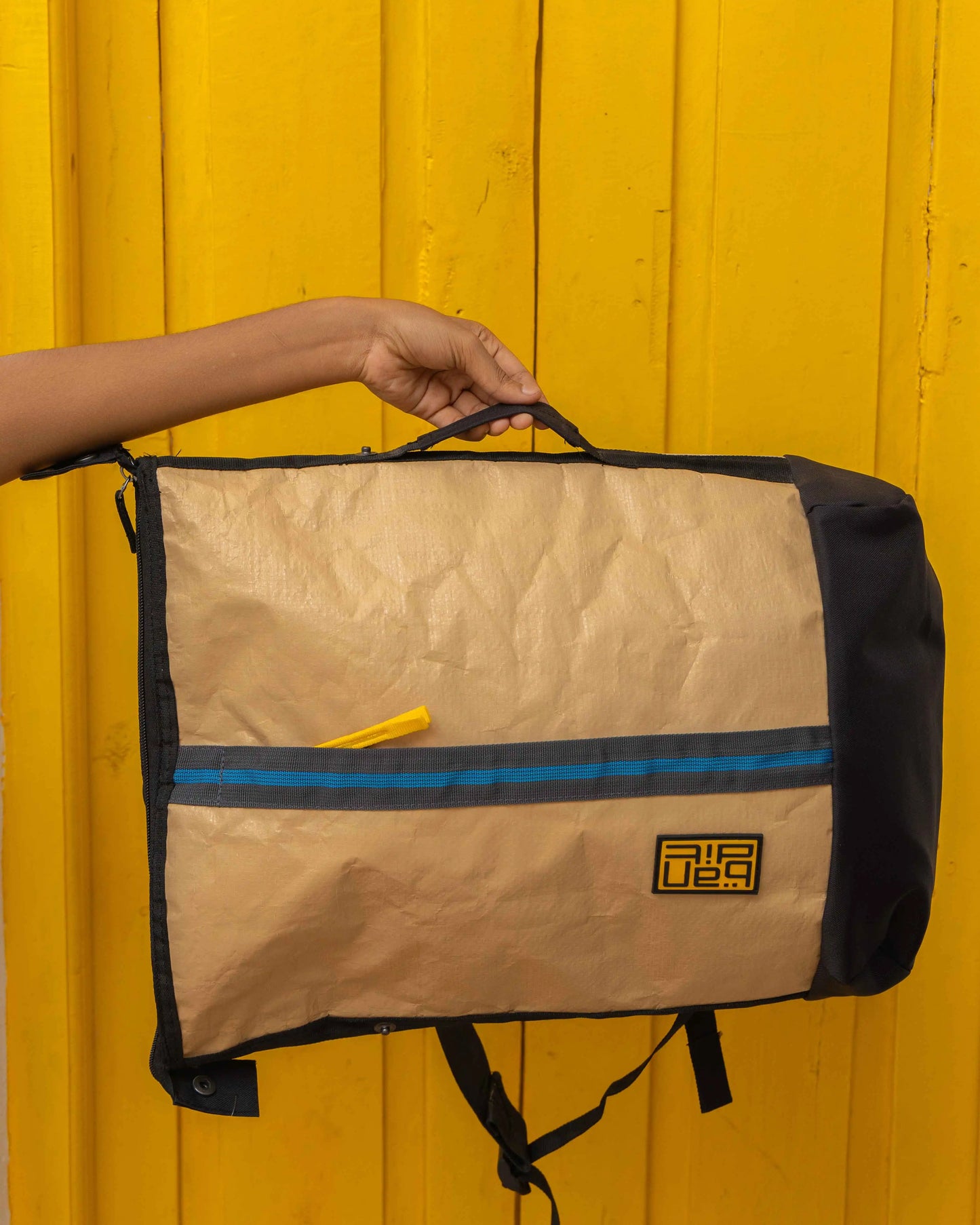 Person holding NAD's bag for men, set against a bright yellow backdrop, highlighting the paper backpack design. 