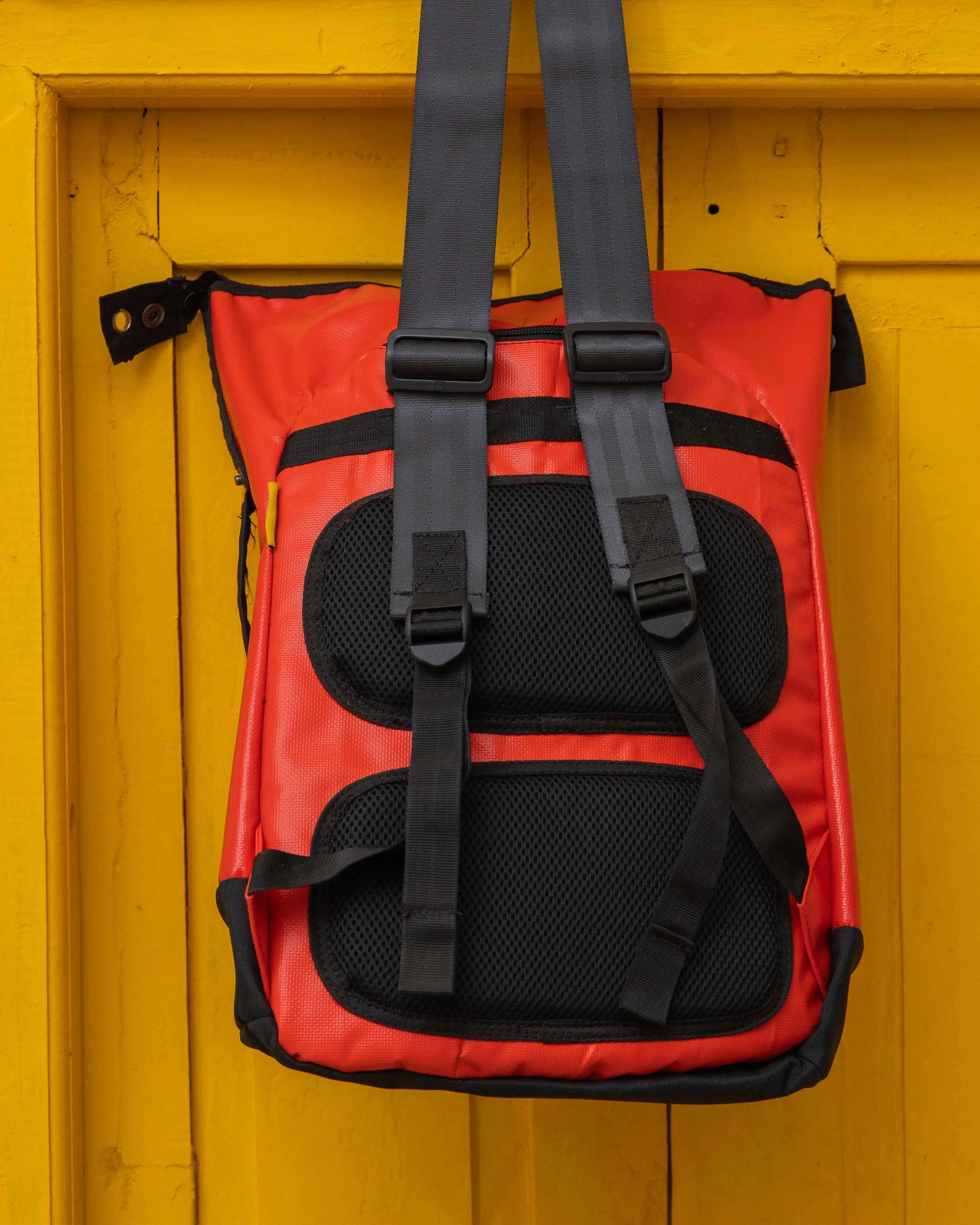 A red and black coloured NAD's backpack for men displayed hanging on a yellow door.